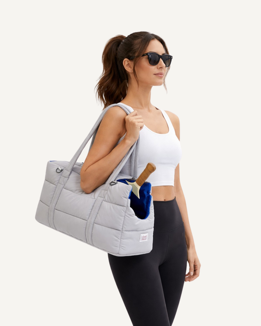 Model holding an aesthetic Good Mess light grey puffer multi-purpose pet carrier with a pickleball paddle