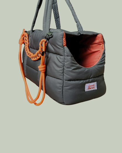 Dark olive green puffer pet carrier with comfortable padded orange interior and U-cut side opening for pets and long shoulder strap for strength and comfort. Aesthetic woven strap handle.