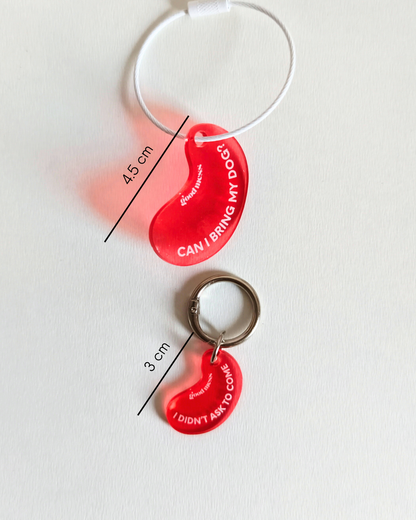 Twinning red acylic bean-shaped pet collar charm with funny text "Can I bring my dog?" and matching bag charm "I didnt ask to come" by Good Mess. For cats and dogs.