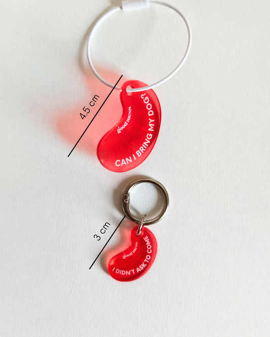 Twinning red acylic bean-shaped pet collar charm with funny text "Can I bring my dog?" and matching bag charm "I didnt ask to come" by Good Mess. For cats and dogs.